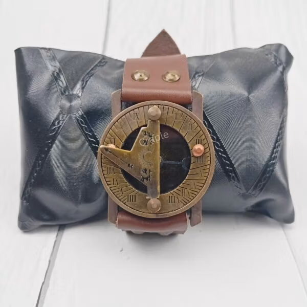 The vintage brass and leather wrist sundial displayed on a black cushion, perfect as a gift item.