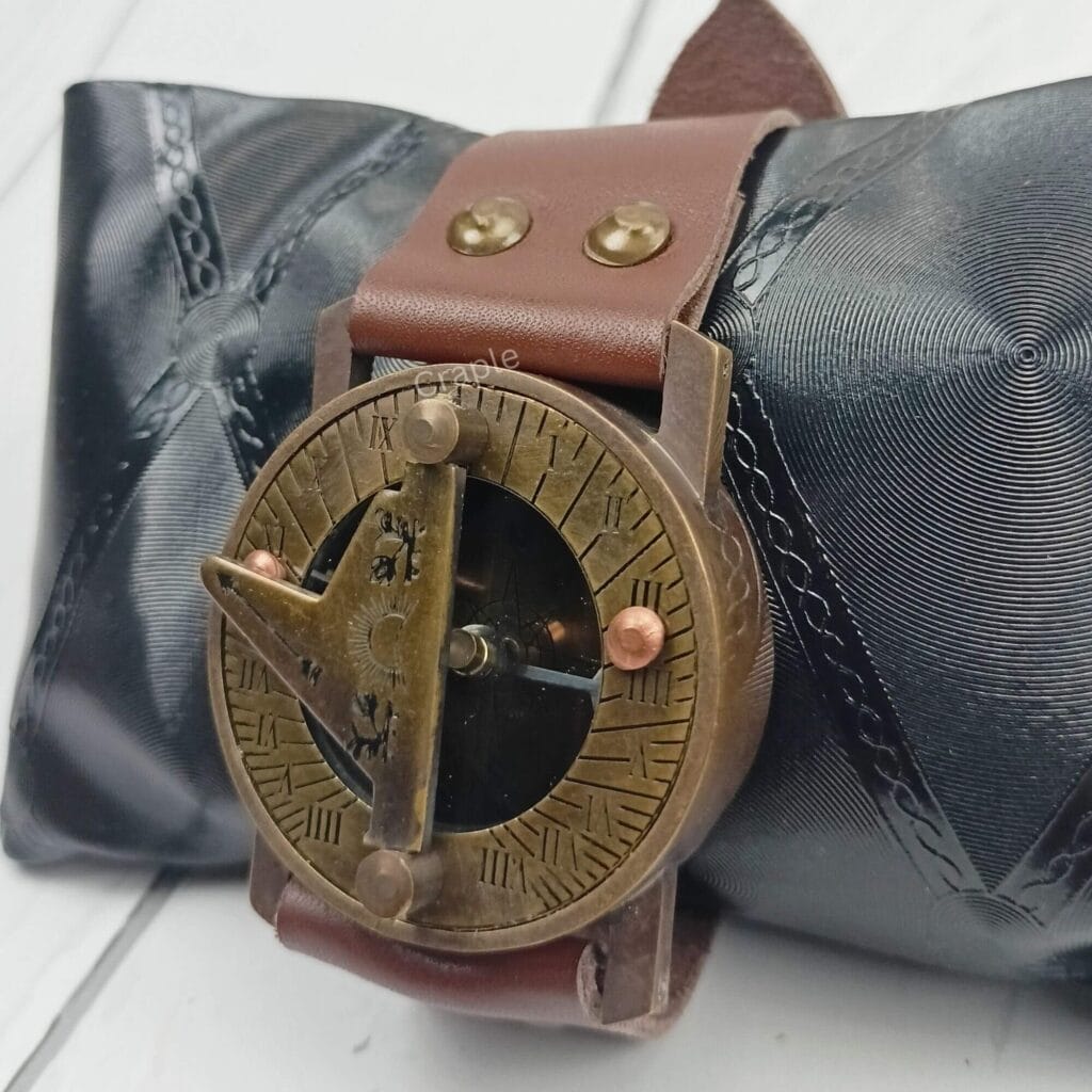 Antique brass wrist sundial compass with a brown leather strap, displayed elegantly on a black cushion.