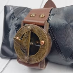 Antique brass wrist sundial compass with a brown leather strap, displayed elegantly on a black cushion.