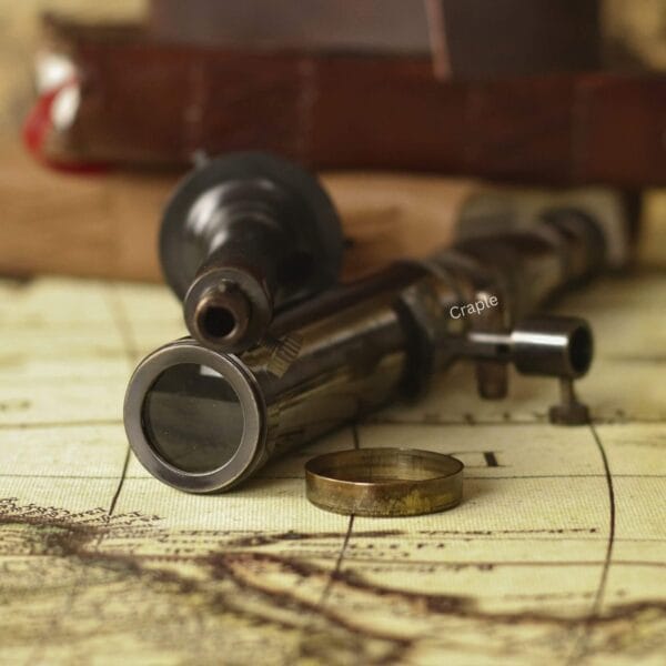 The detachable brass telescope tube lying on a vintage map next to its tripod base and lens cap.