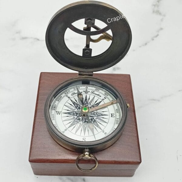 Open antique brass sundial compass with a black finish, displayed inside its polished wooden storage box.