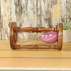 The rosewood 60-minute hourglass resting horizontally on a wooden table, showcasing its handcrafted wooden pillars.