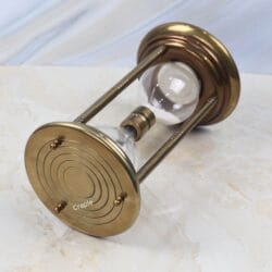 Tilted view of the antique brass hourglass, showing the detailed concentric circles on the base plate.