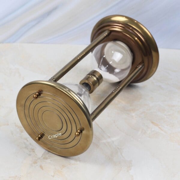 Tilted view of the antique brass hourglass, showing the detailed concentric circles on the base plate.