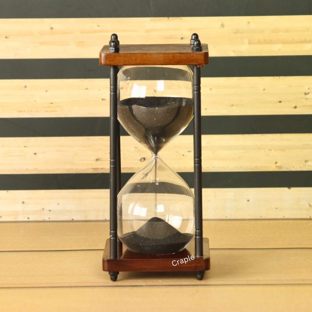 A vintage-style 10-minute hourglass with black sand, a dark wood frame, and black antique brass pillars.