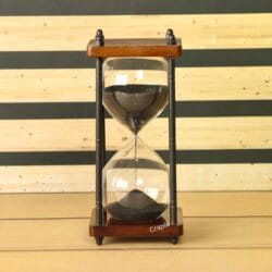 A vintage-style 10-minute hourglass with black sand, a dark wood frame, and black antique brass pillars.