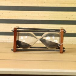 The wooden and antique brass hourglass resting horizontally on a wooden surface, showing the black sand inside.
