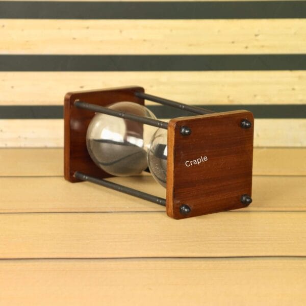 Close-up of the wooden base and antique brass pillars of the 10-minute black sand hourglass.