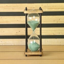 A rustic 10-minute hourglass with dark green sand, framed by natural wood and black antique-finish brass pillars.