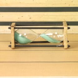 The natural wood and brass sand timer resting horizontally on a wooden surface, showing the green sand inside.