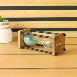 The wood and brass sand timer displayed as a decorative piece on a desk next to a small plant.