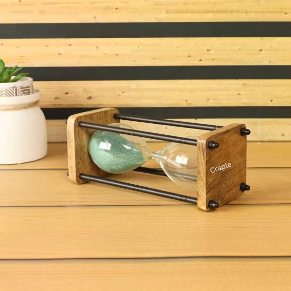 The wood and brass sand timer displayed as a decorative piece on a desk next to a small plant.