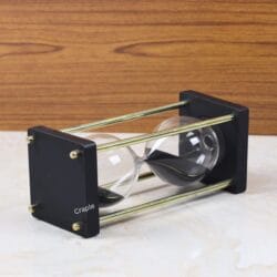 The black wood and nickel brass hourglass resting horizontally on a marble surface, showing the black sand settled in the glass.