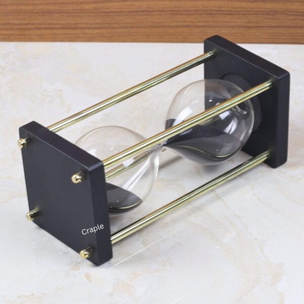 Close-up angled view of the modern sand timer, highlighting the contrast between the black wood base and shiny brass pillars.