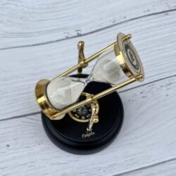 A rotating 3-minute hourglass with a polished brass frame and white sand, mounted on an engravable black wooden base with a built-in compass.