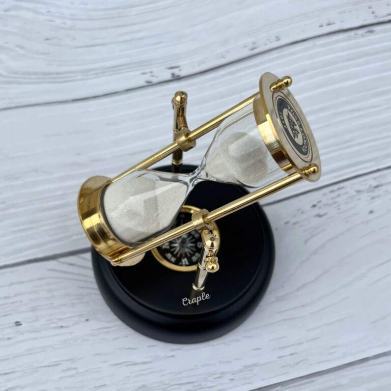A rotating 3-minute hourglass with a polished brass frame and white sand, mounted on an engravable black wooden base with a built-in compass.