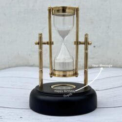 The black wooden base of the hourglass showing the customizable with a "Happy Birthday" message, demonstrating it is engravable.