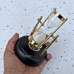 The rotating brass hourglass with compass base held in a person's hand to demonstrate its size and scale.