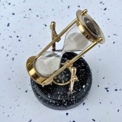 The brass hourglass swiveling on its axis, demonstrating the rotating feature over the wooden base.