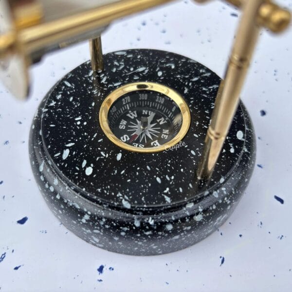 A close-up of the black wooden base, showing the marble-like finish and the detailed brass compass set within it.