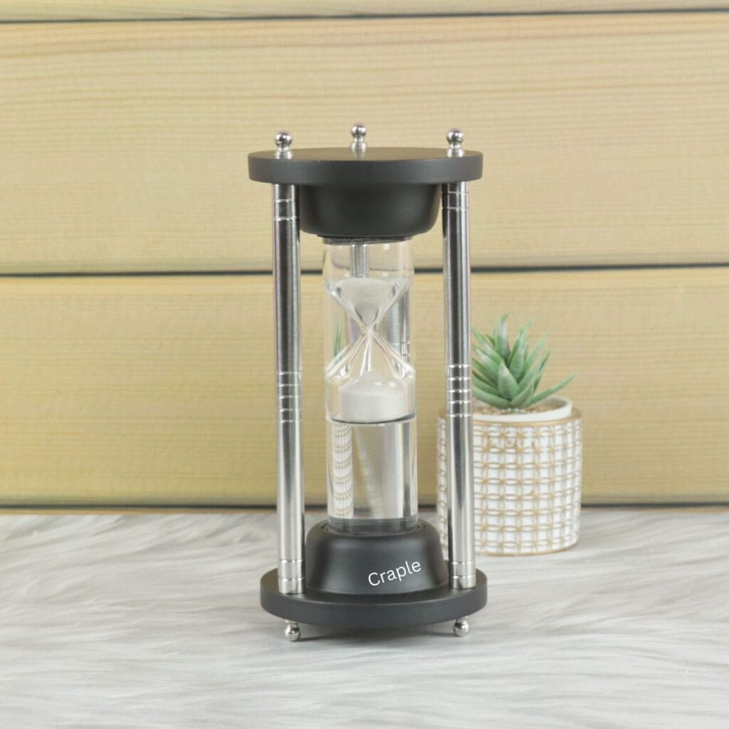 A modern 3-minute floating hourglass with white sand, a black frame, and polished steel pillars.