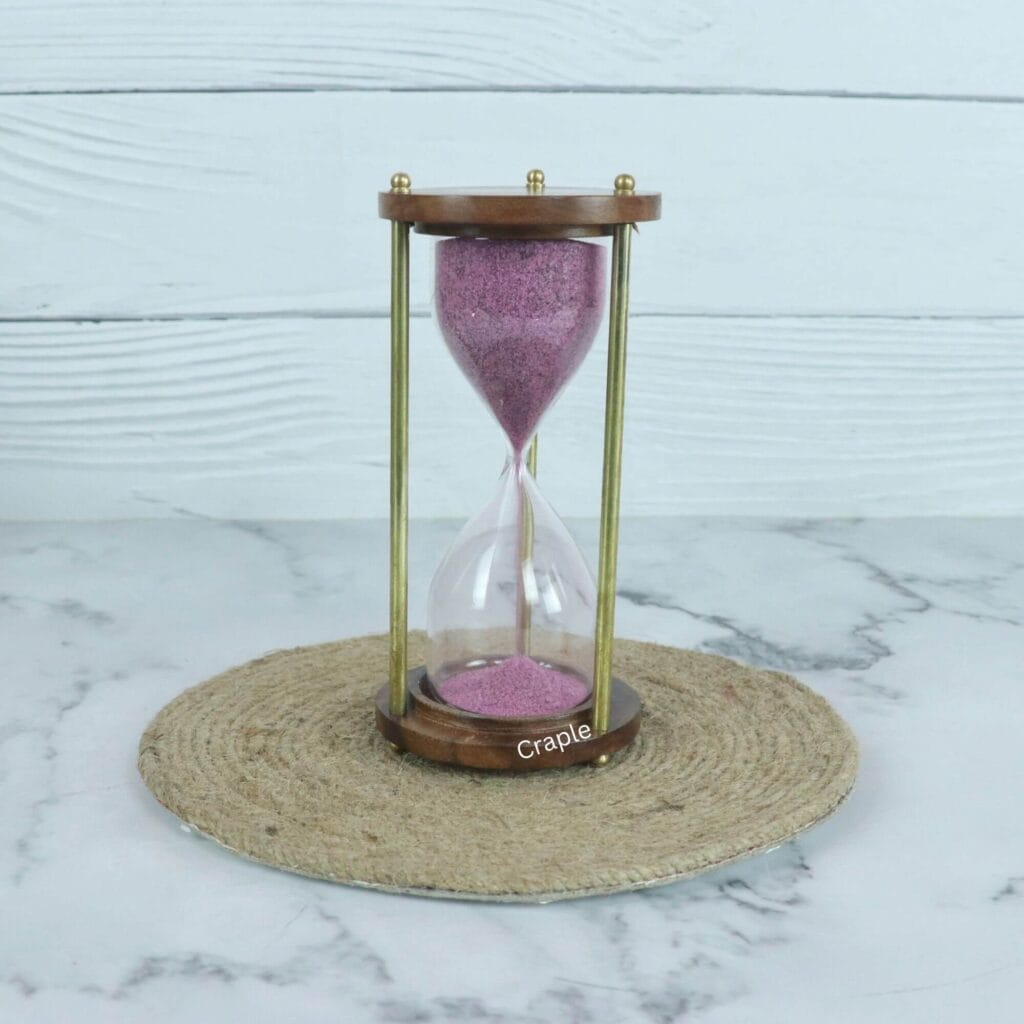 A vintage 3-minute hourglass with purple sand, framed by round wooden bases and classic brass pillars.