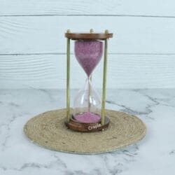 A vintage 3-minute hourglass with purple sand, framed by round wooden bases and classic brass pillars.