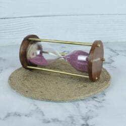 The wooden and brass 3-minute sand timer resting horizontally, showcasing its classic design and purple sand.