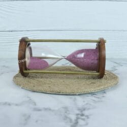 Side profile of the vintage hourglass, showing the purple sand flowing between the glass bulbs within the brass frame.
