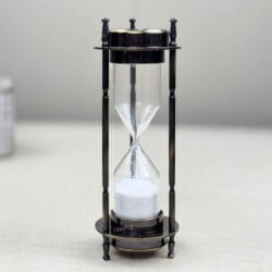 Front view of an antique brass 3-in-1 desktop accessory, focusing on the 3-minute white sand hourglass.