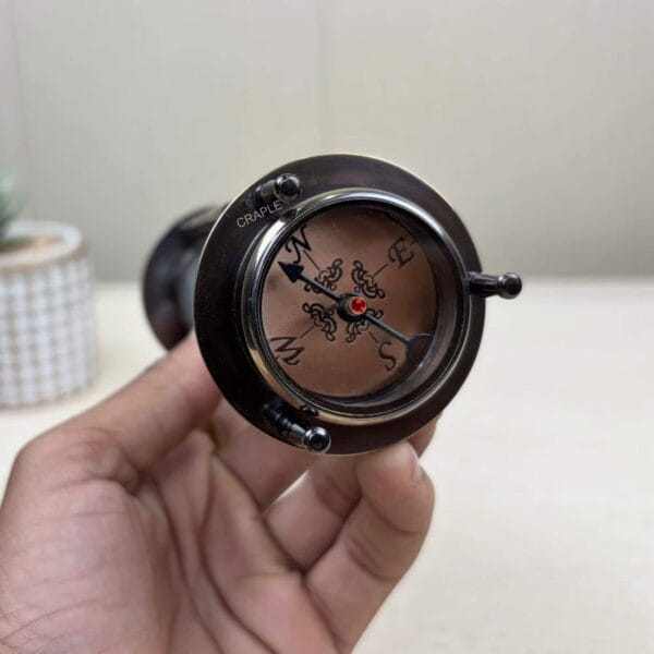 The bottom of the 3-in-1 hourglass held in hand, revealing the integrated antique-style compass.