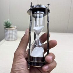 The antique brass hourglass and clock being held to demonstrate its size and portability.