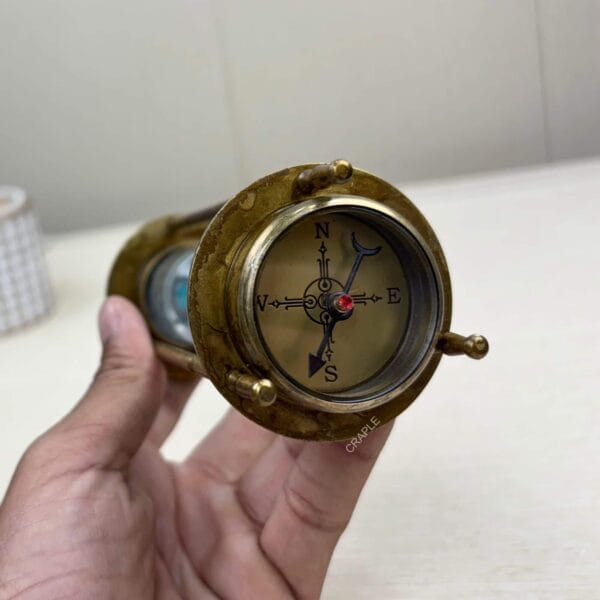 Close-up of the antique brass compass on the end of a 3-in-1 hourglass, held in a hand.