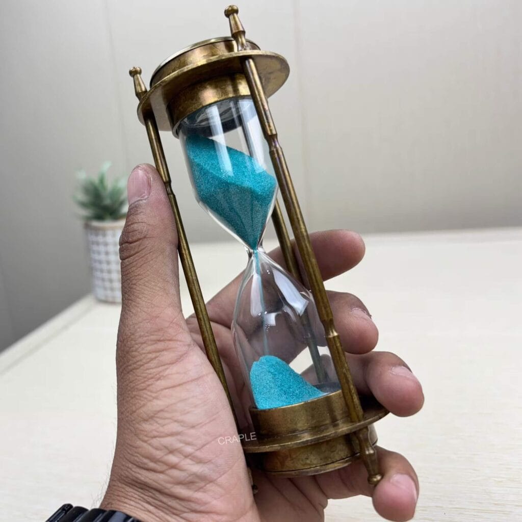 A 3-in-1 antique brass hourglass with blue sand held in a hand to show its size and craftsmanship.