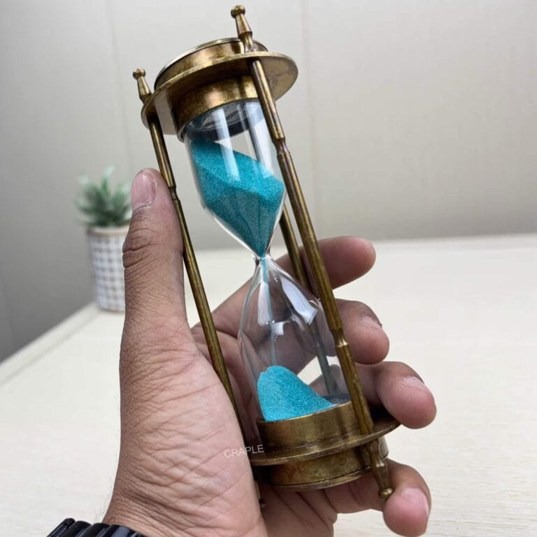 A 3-in-1 antique brass hourglass with blue sand held in a hand to show its size and craftsmanship.
