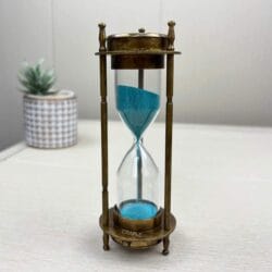 The complete antique brass hourglass standing on a white surface, displaying the vibrant blue sand.