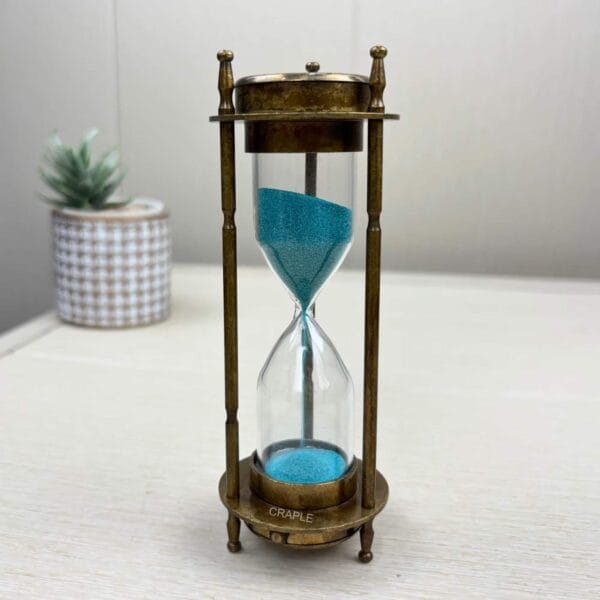 The complete antique brass hourglass standing on a white surface, displaying the vibrant blue sand.