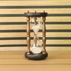 A large 30-minute hourglass with white sand, framed by black wooden bases and antique-finish copper pillars.