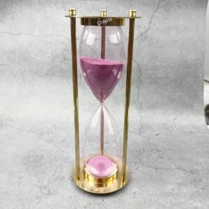 Elegant 30-minute hourglass sand timer featuring a polished brass frame and vibrant light pink sand.