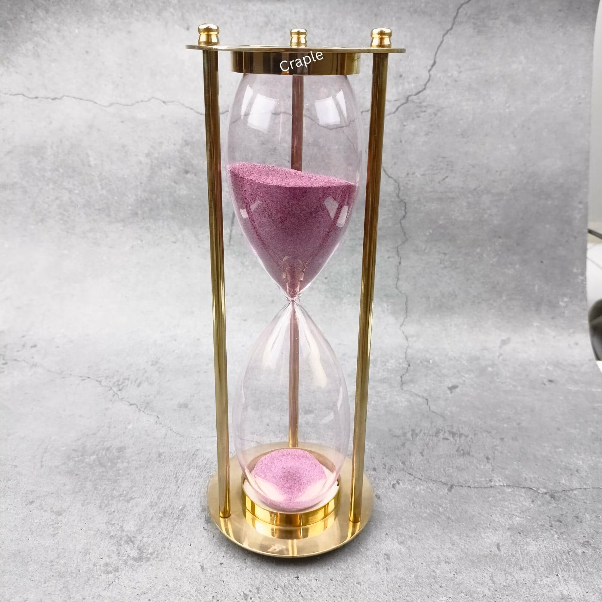Elegant 30-minute hourglass sand timer featuring a polished brass frame and vibrant light pink sand.