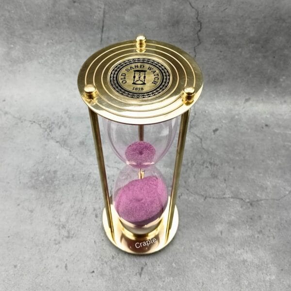 Top view of the brass hourglass, showing the "Old Sand Watch" engraved compass rose design on the top plate.