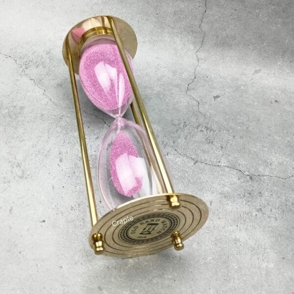 Angled profile of the large brass and glass sand timer with light pink sand.