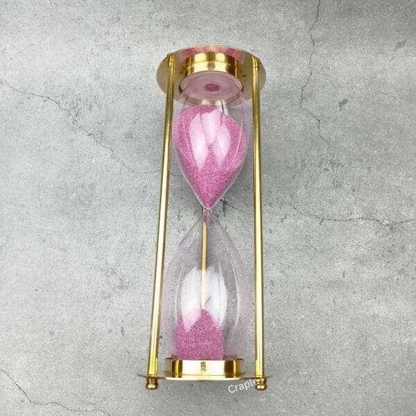 The 30-minute brass hourglass shown after the pink sand has fully flowed to the bottom bulb.