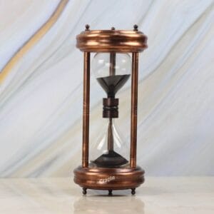 A 5-minute hourglass with an antique copper finish steel frame and black sand, standing on a marble surface.