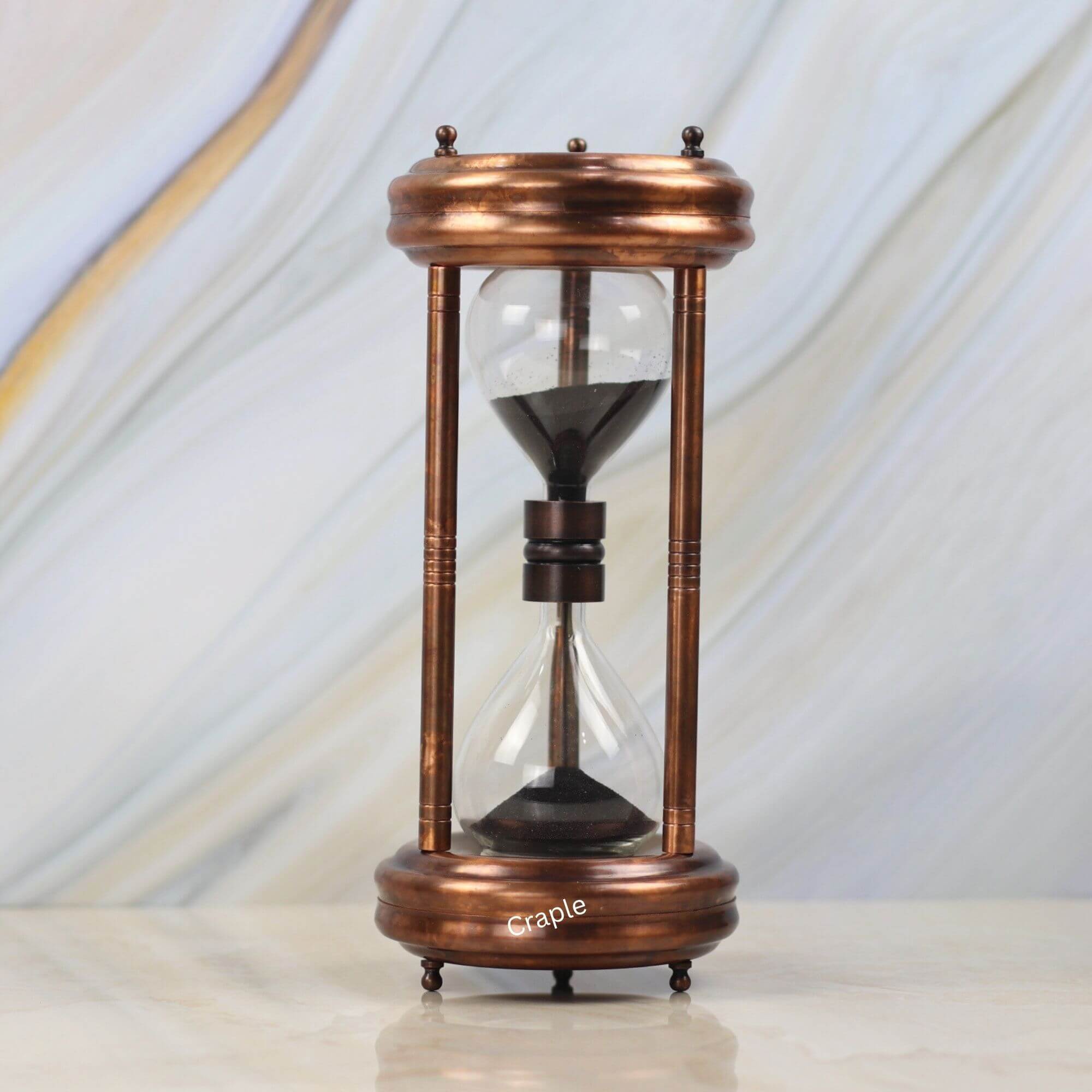 5 Min Antique Copper Finish Steel Hourglass-1 A 5-minute hourglass with an antique copper finish steel frame and black sand, standing on a marble surface.