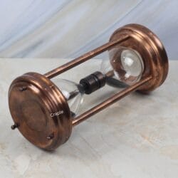 The antique copper sand timer lying on its side, showing the detail of the steel pillars and top plate.