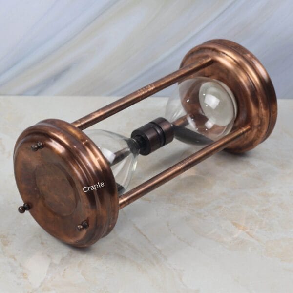 The antique copper sand timer lying on its side, showing the detail of the steel pillars and top plate.