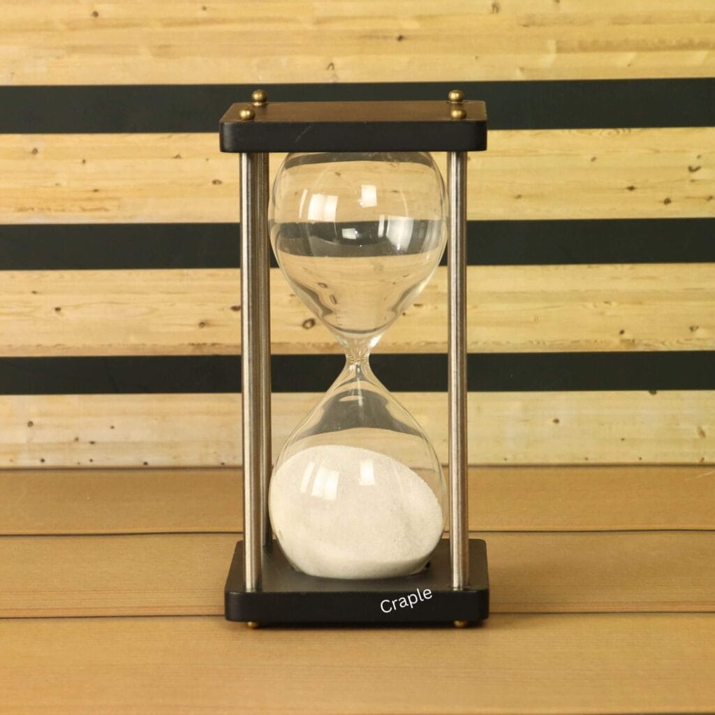 A modern 5-minute hourglass with white sand, a black wooden frame, and nickel-finish brass pillars.