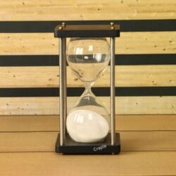A modern 5-minute hourglass with white sand, a black wooden frame, and nickel-finish brass pillars.