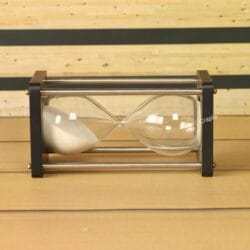 The black wood and nickel brass hourglass resting horizontally, showing the white sand and its sturdy frame.